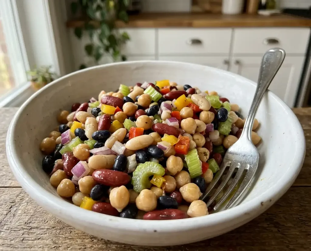 Dense Bean Salad Recipes 2 Classic dense bean salad in a white bowl with mixed beans, diced vegetables, and shiny vinaigrette dressing on a modern kitchen counter